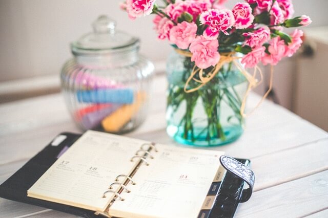 A notepad sitting on a wooden desk with a vase and pink flowers in the background