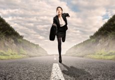 woman running down the centre of a rod towards the camera in a business suit and with a briefcase