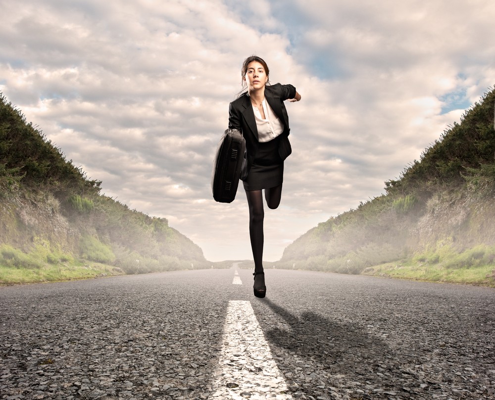 woman running down the centre of a rod towards the camera in a business suit and with a briefcase