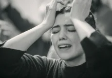 A woman looking exasperated holding her hands to her forehead with her eyes closed