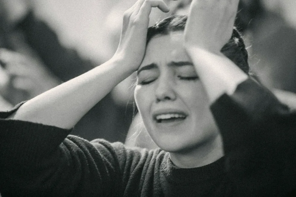 A woman looking exasperated holding her hands to her forehead with her eyes closed