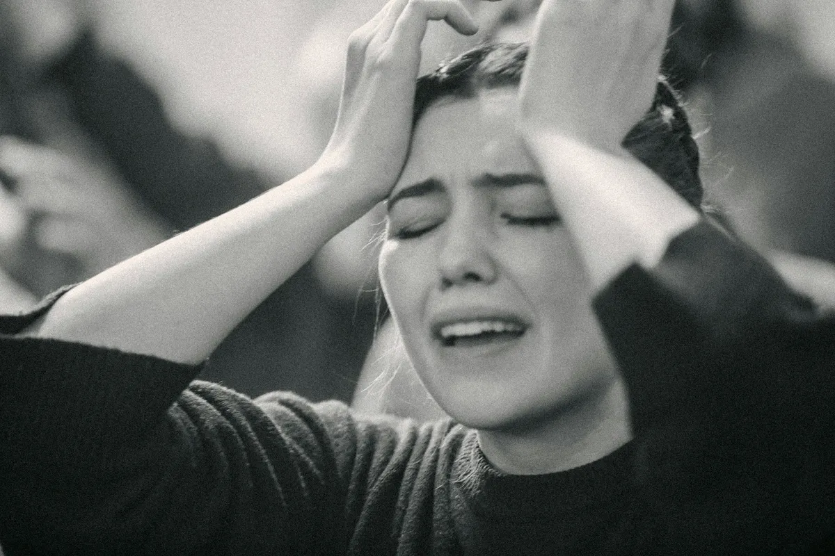 A woman looking exasperated holding her hands to her forehead with her eyes closed