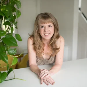 Jilly Wootton sat at a desk smiling with a hanging green plant next to her